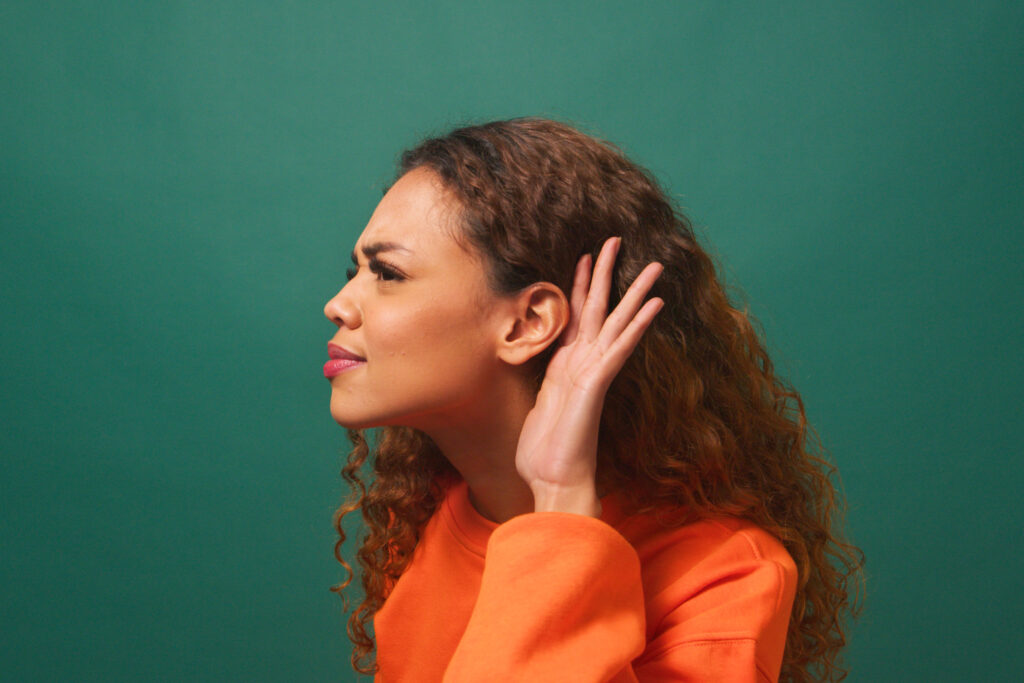 Young biracial woman cups ear, listening intently, green studio background. High quality photo